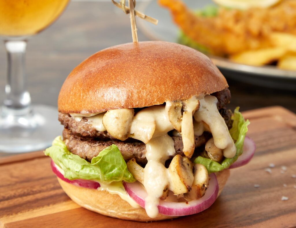 Stilton & Mushroom burger on board with fish and chips in background and pint